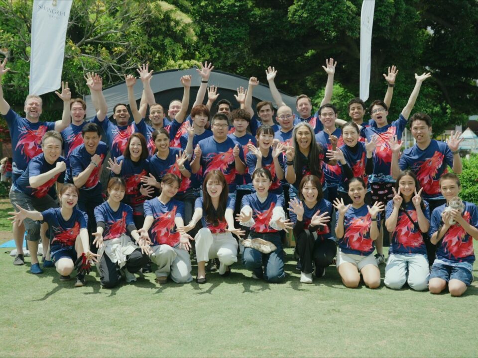 芝生の上で手を挙げて喜ぶ、企業イベント参加者の集合写真