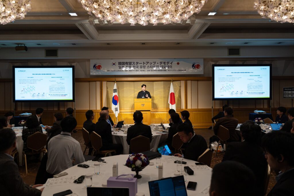 日本と韓国の国旗が並ぶホテルの宴会場で、登壇者の話を聞く参加者たち