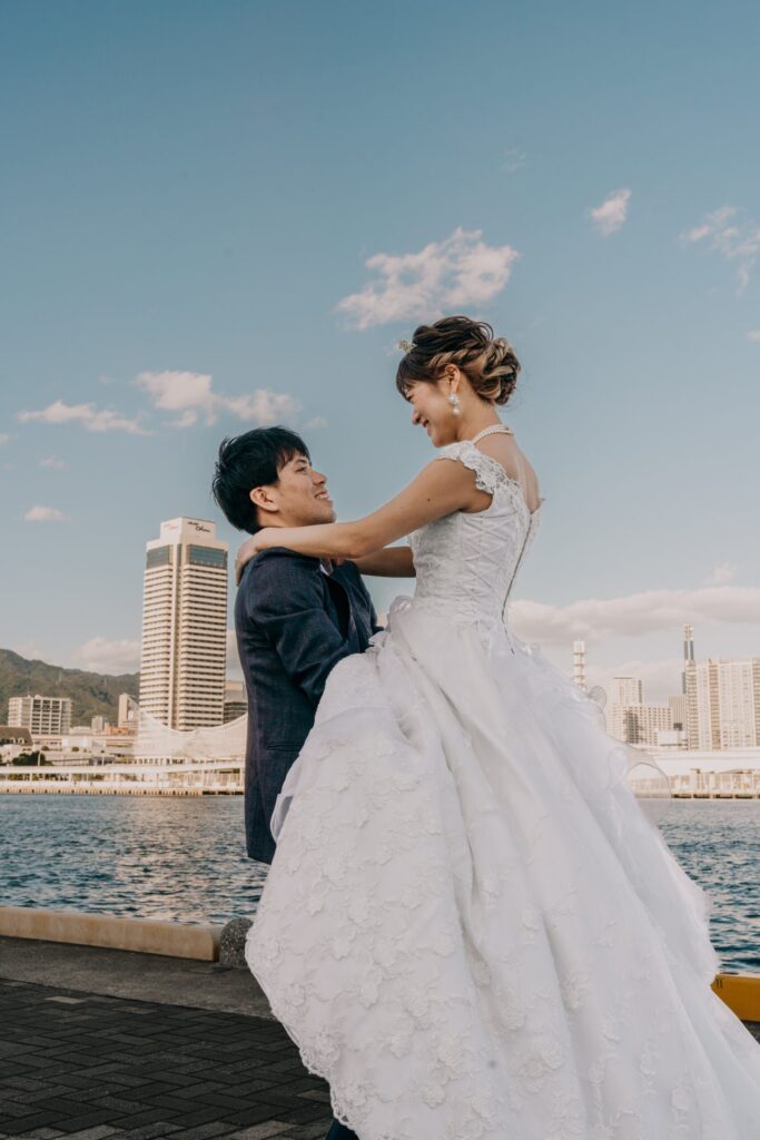 港を望む海辺で、ウェディングドレス姿の新婦と向き合う新郎