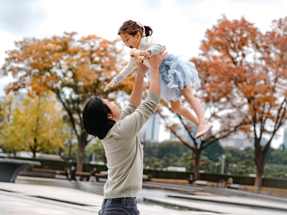 皇居外苑の紅葉を背に、娘を高く抱き上げて笑う父親