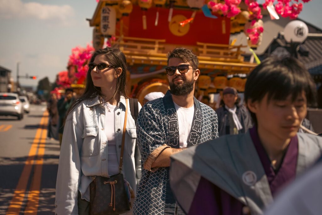 日光の祭りで、山車の前を歩くツアーのゲストと地元の人